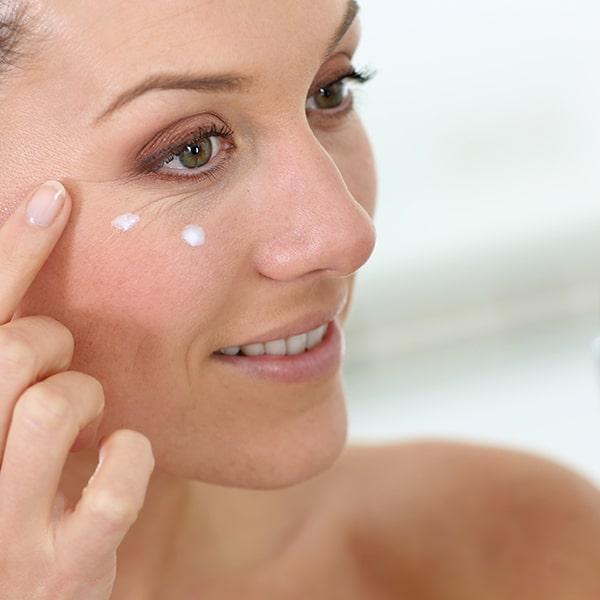 Woman applying small amount of cream near her right eye