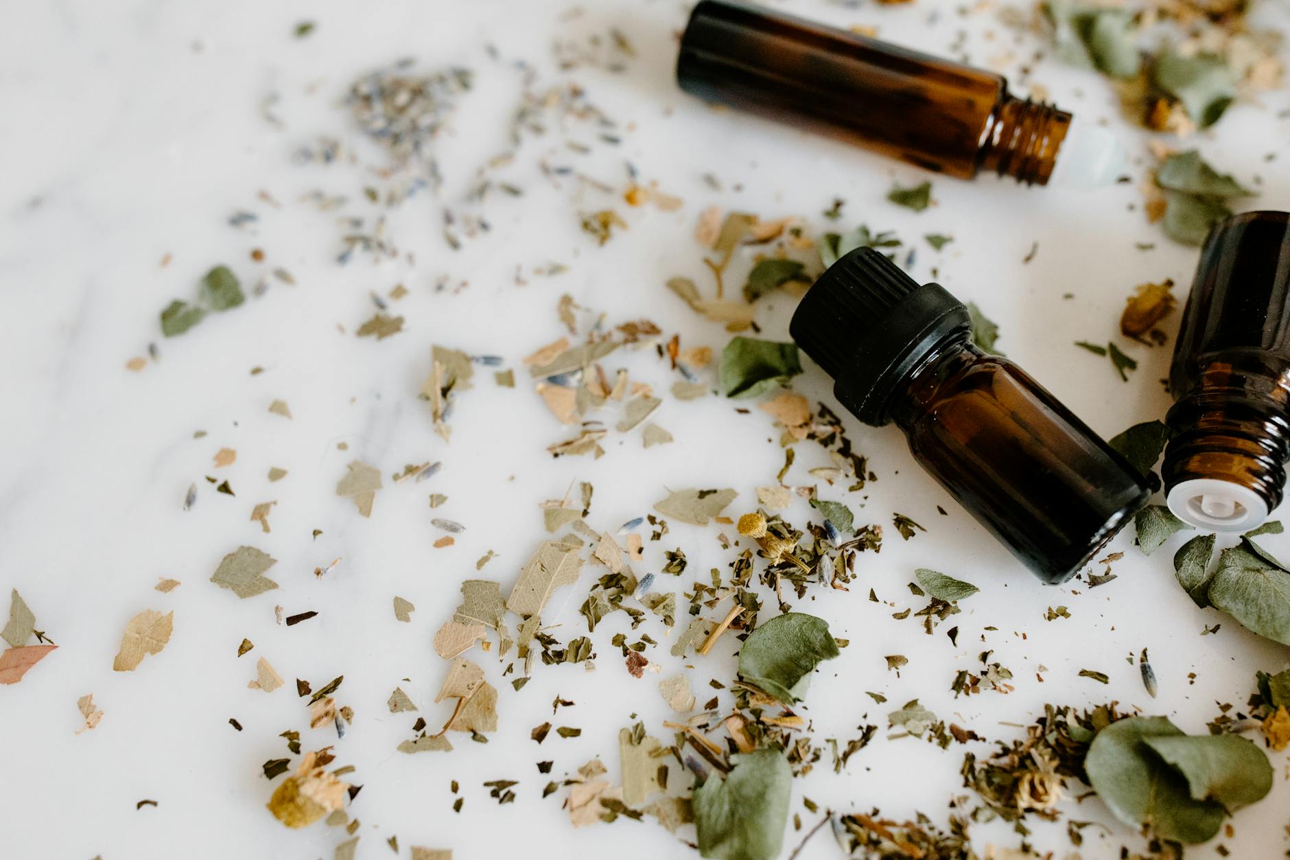 close up shot of essential oil bottles and herbs on white surface